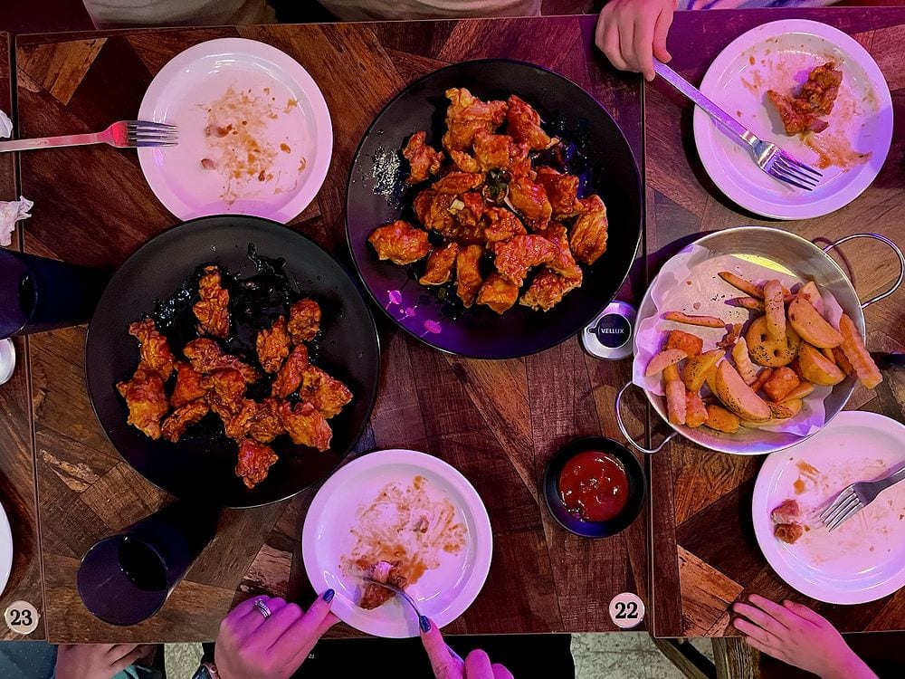 Overhead shot of two plates of Korean fried chicken in soy garlic and spicy glazes with seasoned fries on a wooden restaurant table in Myeongdong