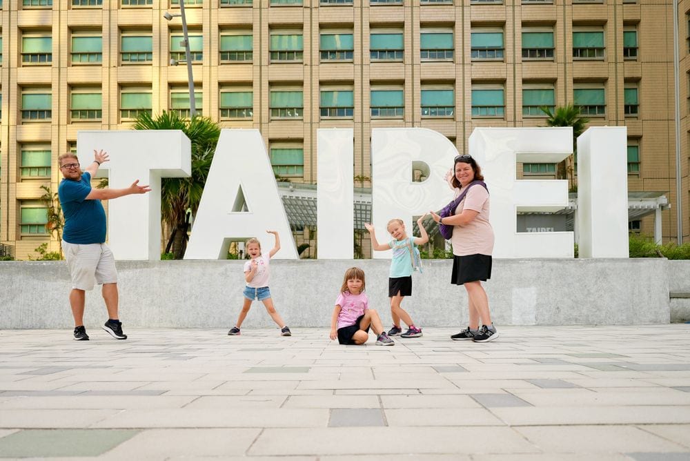 Adam, Lindsay, and their three daughters posing in front of the large white TAIPEI letters.