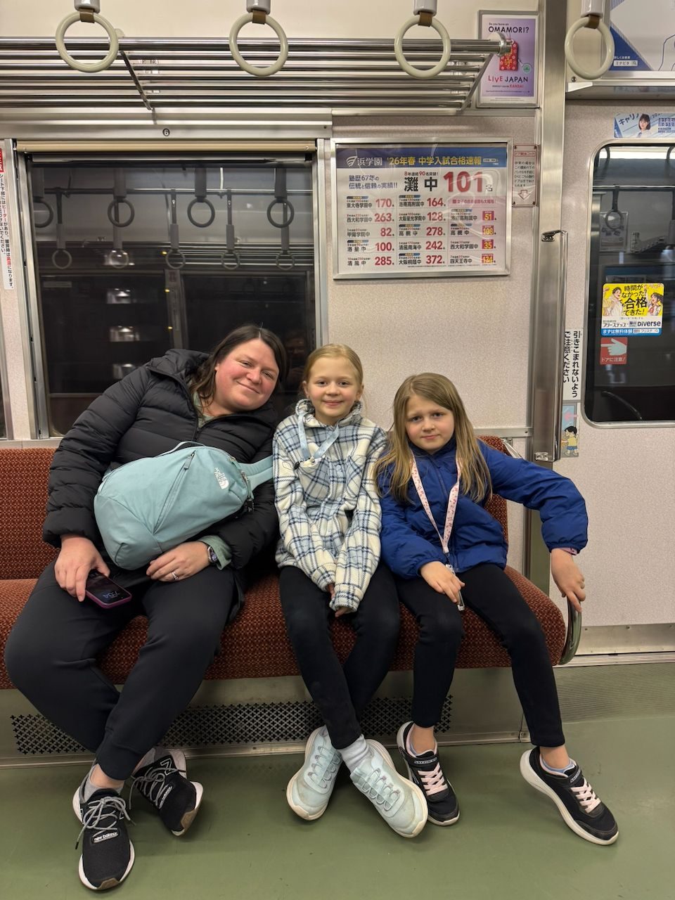 Lindsay, Lily and Cora sitting together on a nearly empty Osaka subway car with Japanese advertisements on the wall behind them