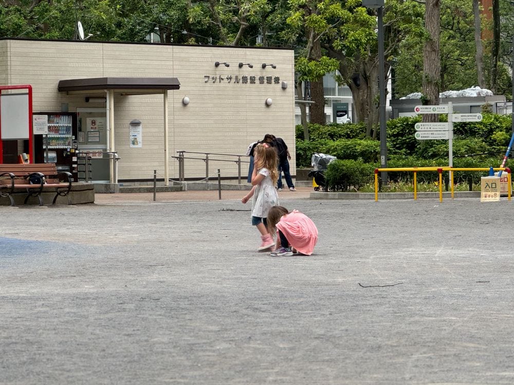 Two young girls play on an open paved plaza in front of a futsal facility in West Shinjuku, Tokyo.