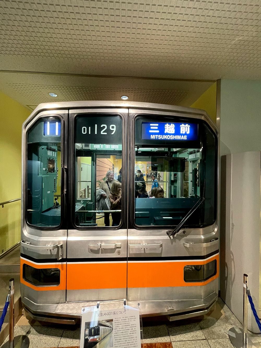 A vintage orange and silver Tokyo Metro subway car on display, front nose visible with a destination sign reading Mitsukoshimae.