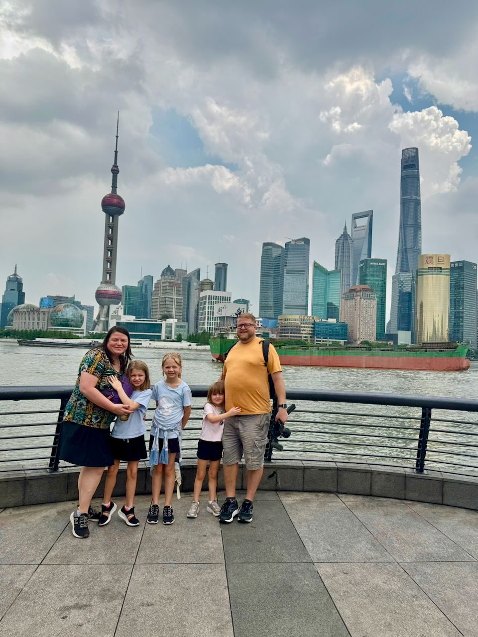 The family of five standing on the Bund promenade in Shanghai with the Pudong skyline and Oriental Pearl Tower behind them