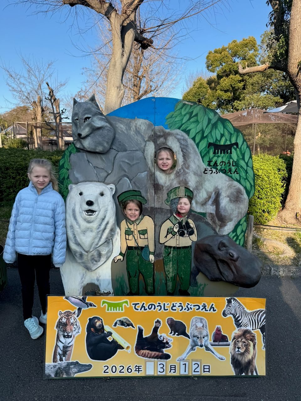 Three girls posing at the Tennoji Zoo entrance photo board, two with their faces through cutouts