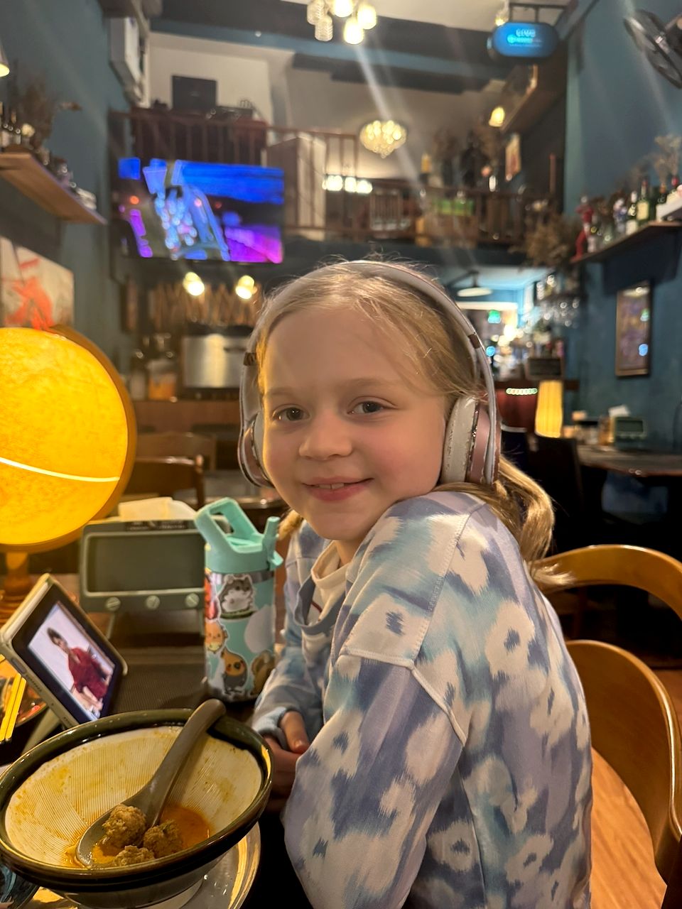 Lily sits at a table at Charm Cafe in Chiang Mai wearing headphones, smiling back at the camera with a nearly finished bowl of khao soi in front of her