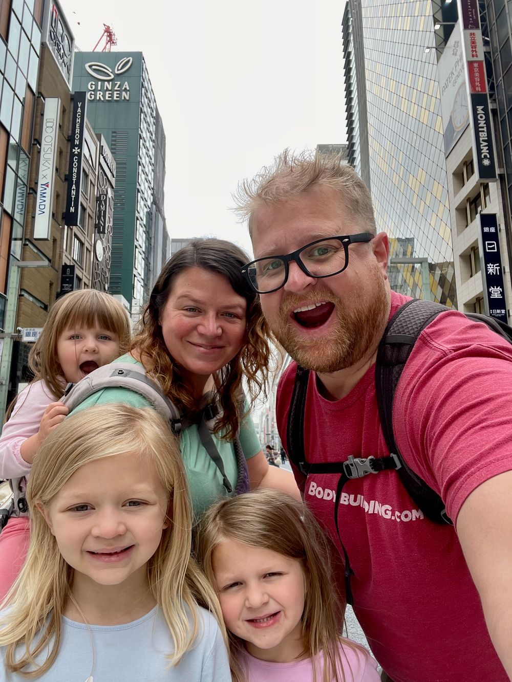 A family of five stands in the middle of a closed-off Ginza street in Tokyo, with the Ginza Green building and luxury storefronts visible behind them.