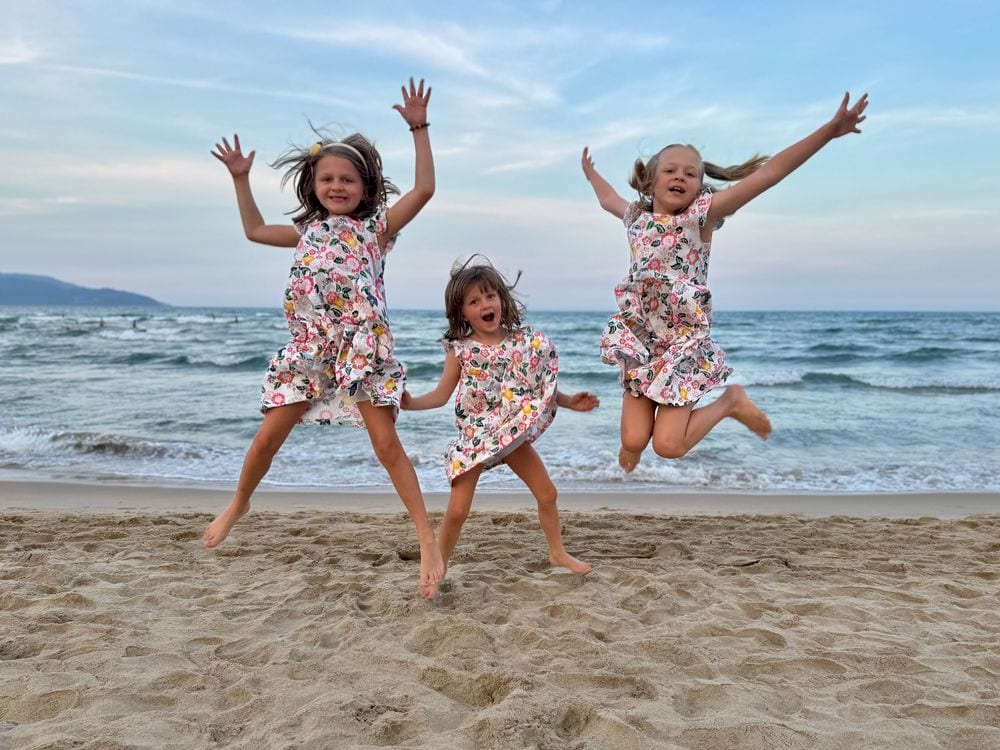 Lily, Cora, and Harper jumping on the beach at My Khe in matching floral dresses