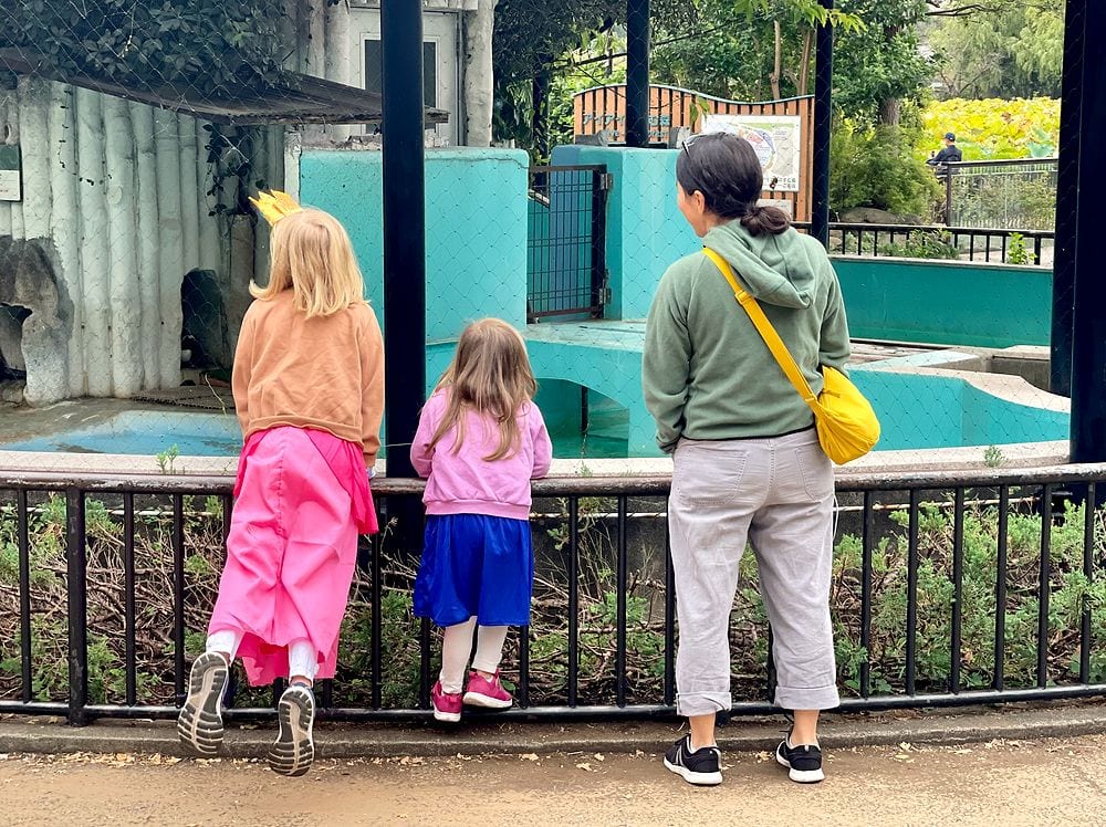 A family of three stands at a railing looking into an animal enclosure at Ueno Zoo in Tokyo.