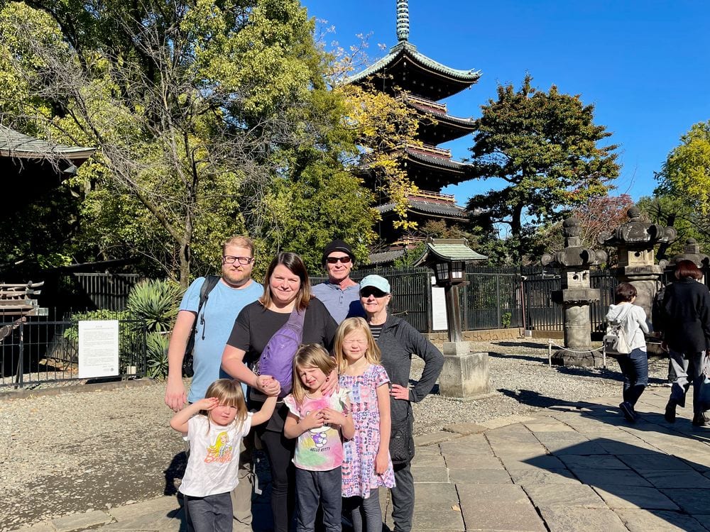 A family of five poses in front of a historic five-story pagoda at Ueno Park on a clear autumn day, surrounded by trees showing fall color.
