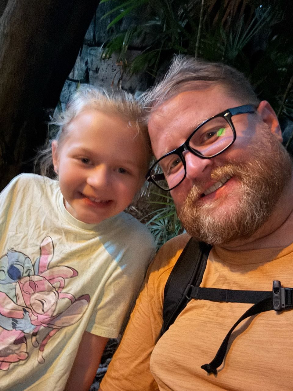 Adam and Lily take a selfie together inside a dark, jungle-themed attraction at Tokyo DisneySea, both smiling at the camera, with Lily wearing a Stitch-themed shirt.