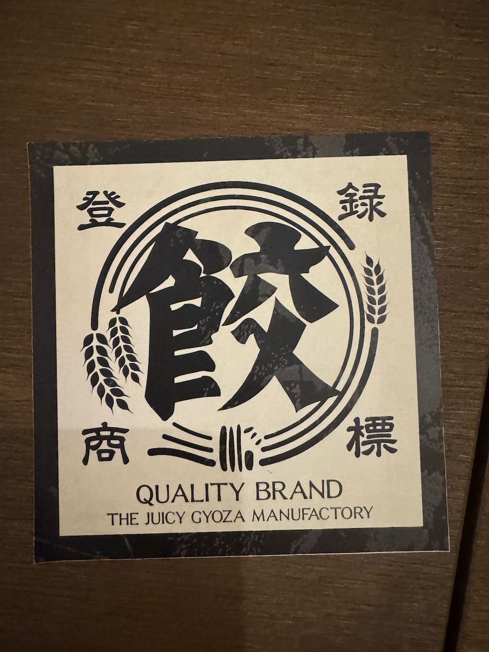 A menu card on a wooden table printed with Japanese kanji and the English text The Juicy Gyoza Manufactory