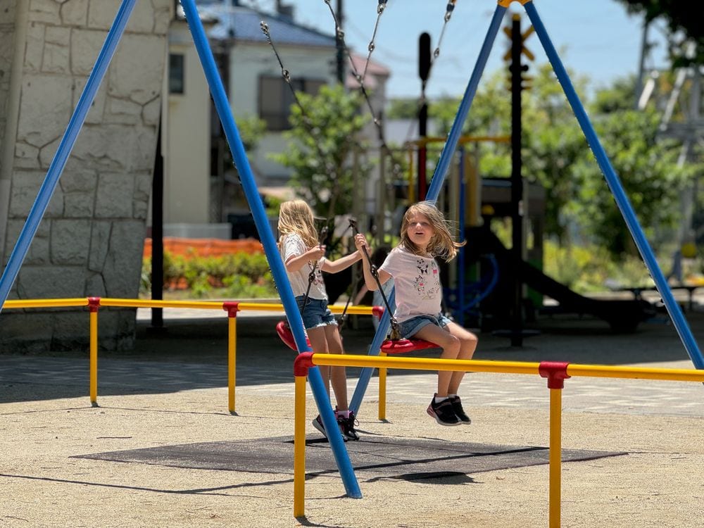 Two young girls play together on a swing set at a neighborhood playground in Katsushika, Tokyo.