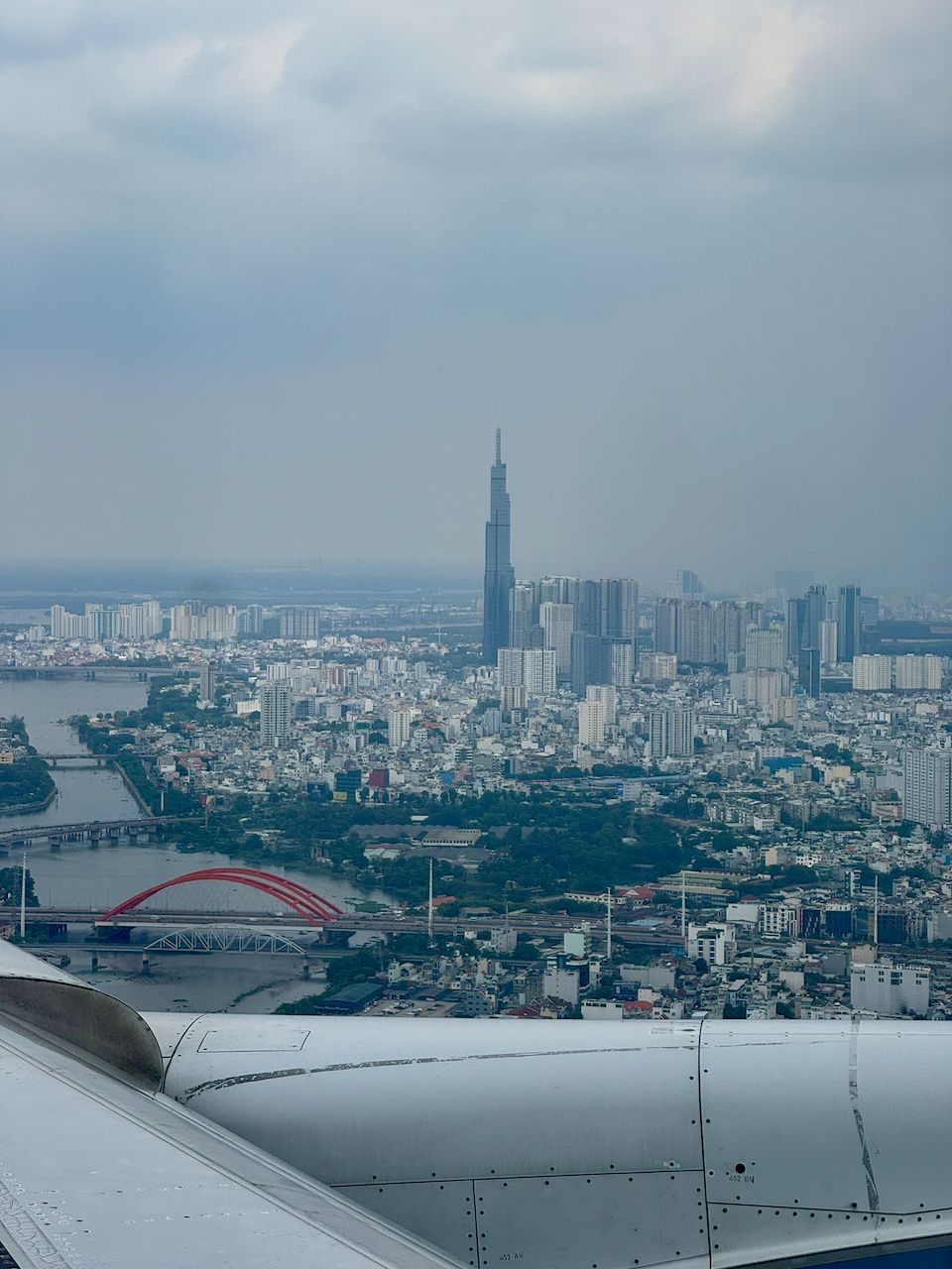View from an aircraft window on approach to Ho Chi Minh City, with Landmark 81 rising through the haze above the Saigon River