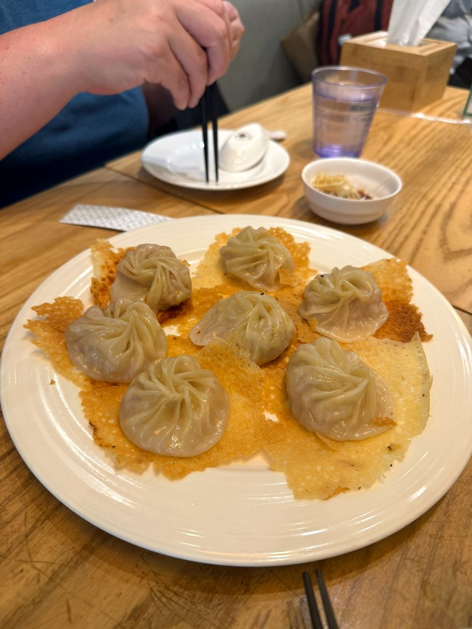 A plate of pan-fried soup dumplings resting on a golden crispy lace crust on a wooden table.