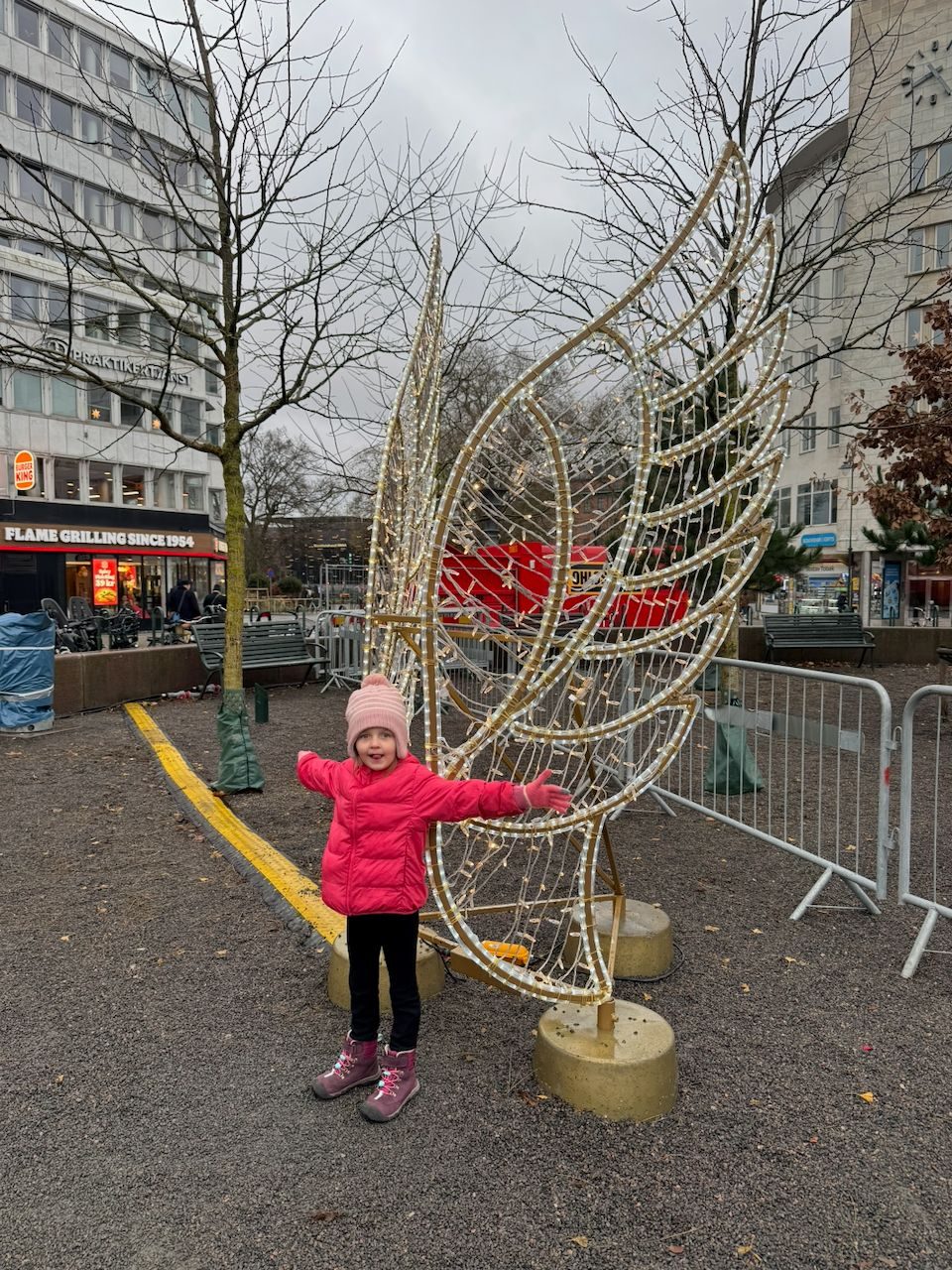 Harper standing with her arms spread wide in front of a large illuminated wings installation in central Malmö
