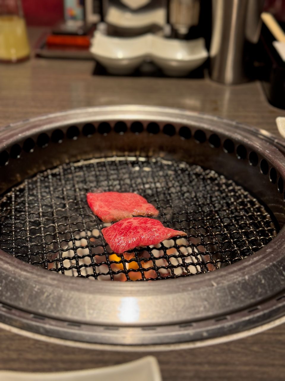 Two small pieces of raw, well-marbled beef sizzling on a round charcoal grill set into a restaurant table in Asakusa, Japan.