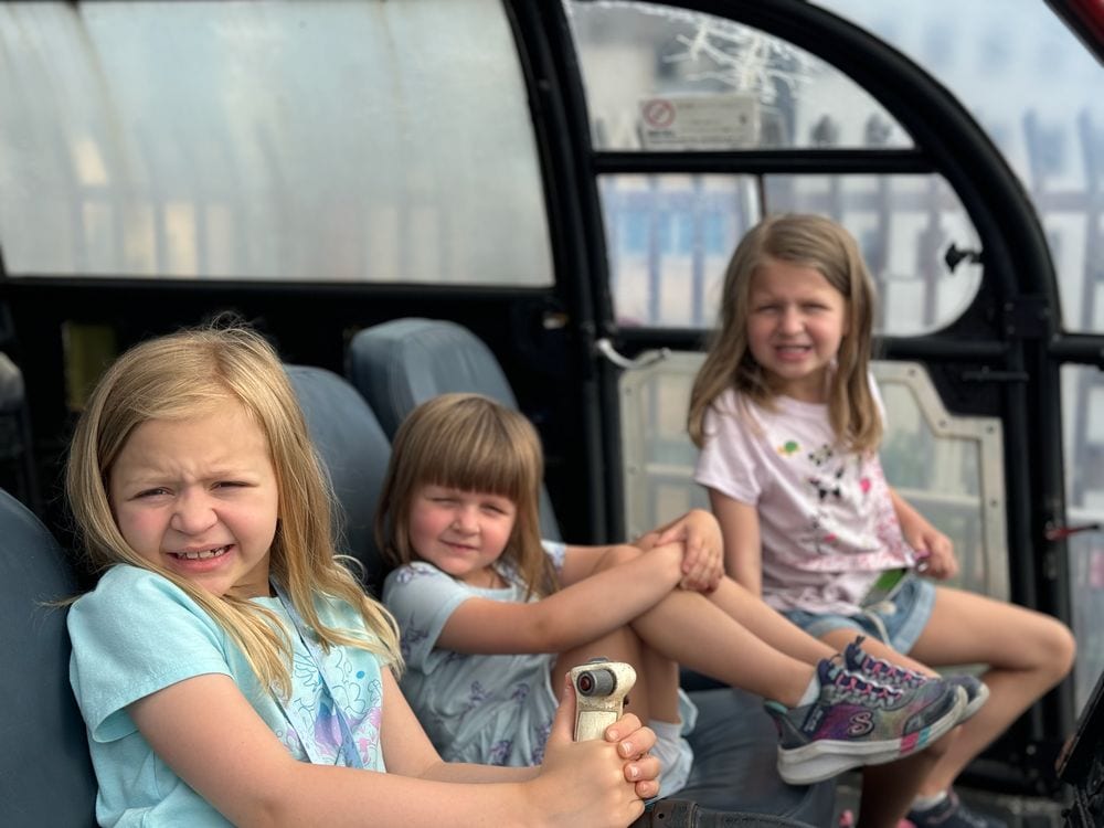 Three young girls sit together inside the open cab of a historic fire vehicle at the Tokyo Fire Museum.