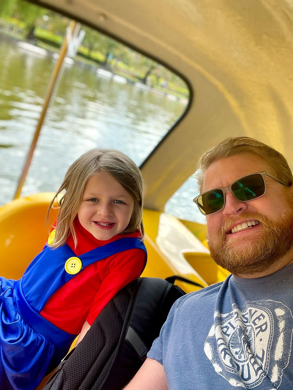 A man and a young girl in a green Luigi costume ride together in a yellow swan-shaped paddle boat on Shinobazu Pond in Ueno Park, Tokyo.