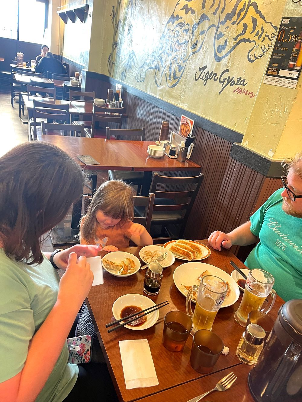 A family eats gyoza at a wooden table in a retro restaurant in Asakusa, Tokyo, with mugs of beer and plates of dumplings spread across the table.