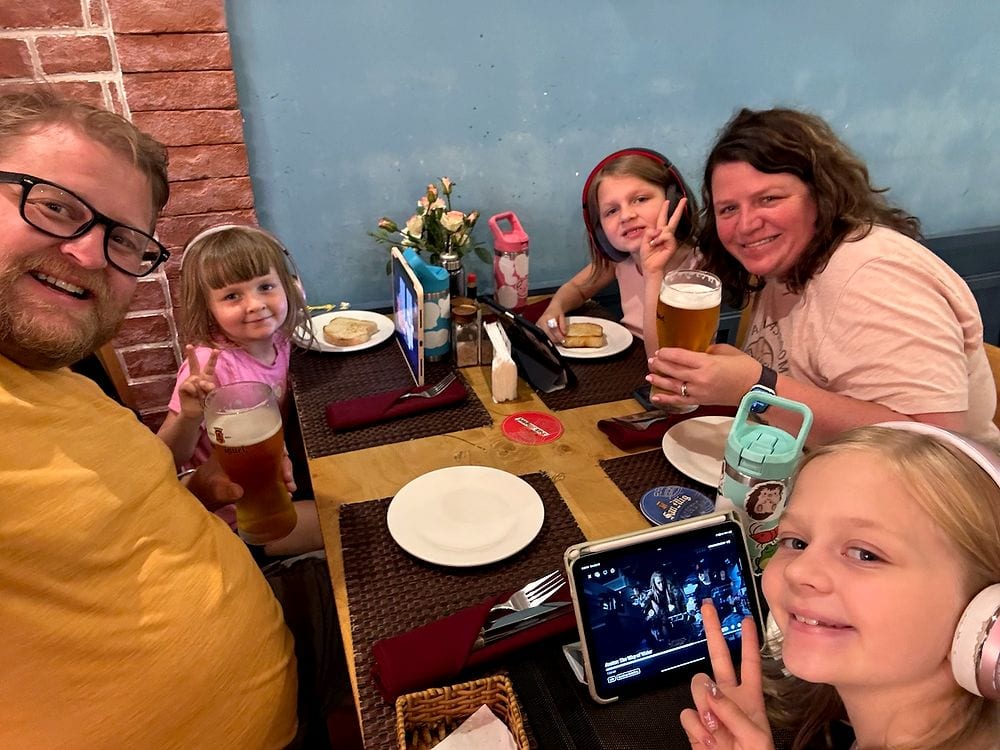 The Clarkson family at a restaurant table in Da Nang, three girls wearing headphones with an iPad propped up in the foreground