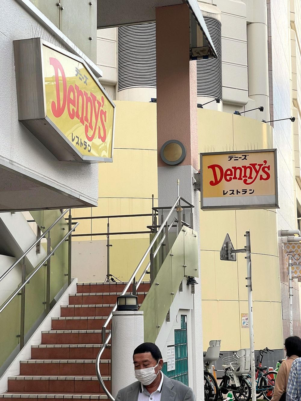 A Denny's restaurant storefront sign in Asakusa, Tokyo, seen from a staircase landing with pedestrians passing below.