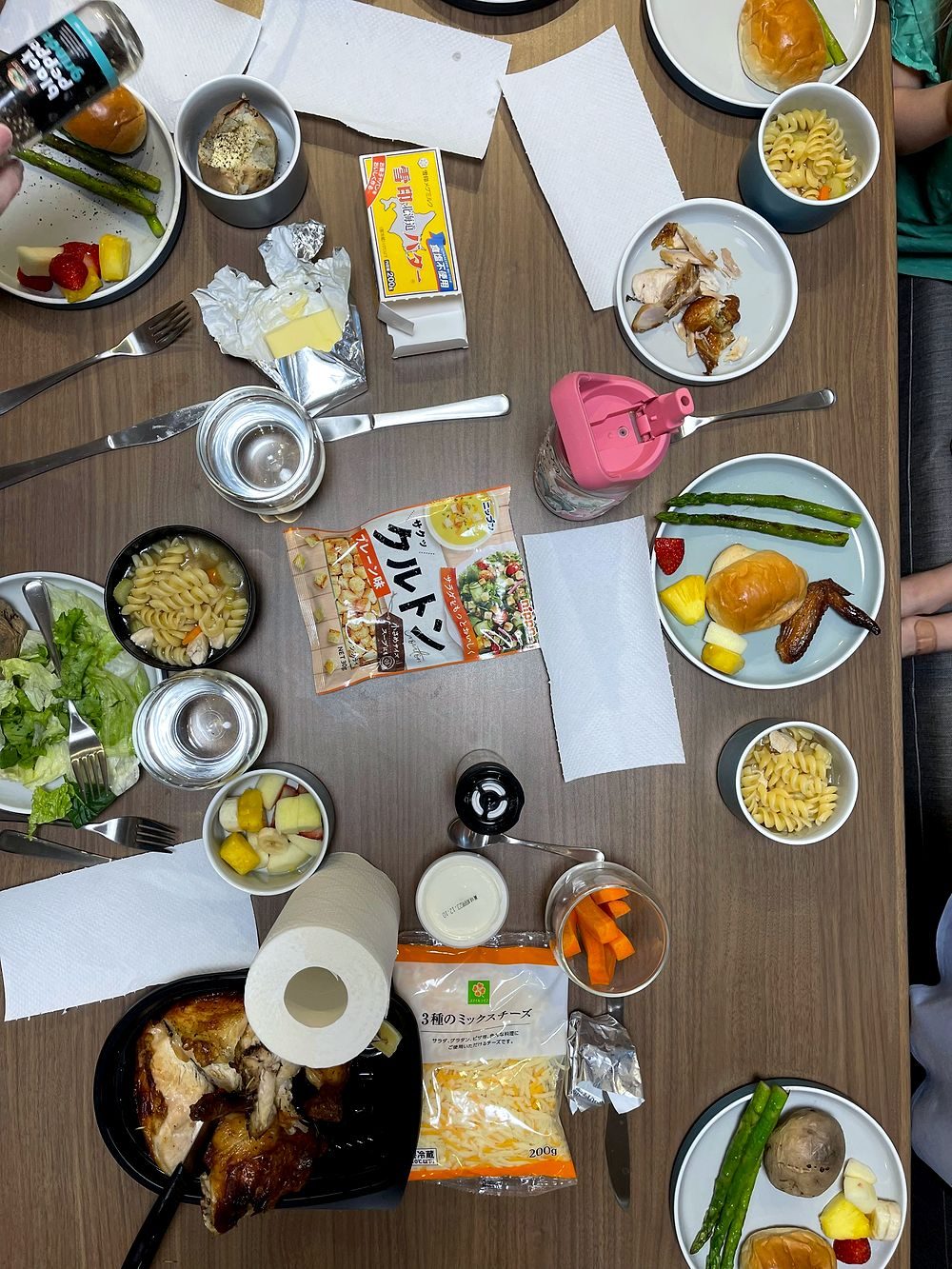A Thanksgiving spread seen from above on a Tokyo apartment table, including roast chicken, baked potatoes, asparagus, pasta salad, and fruit salad.