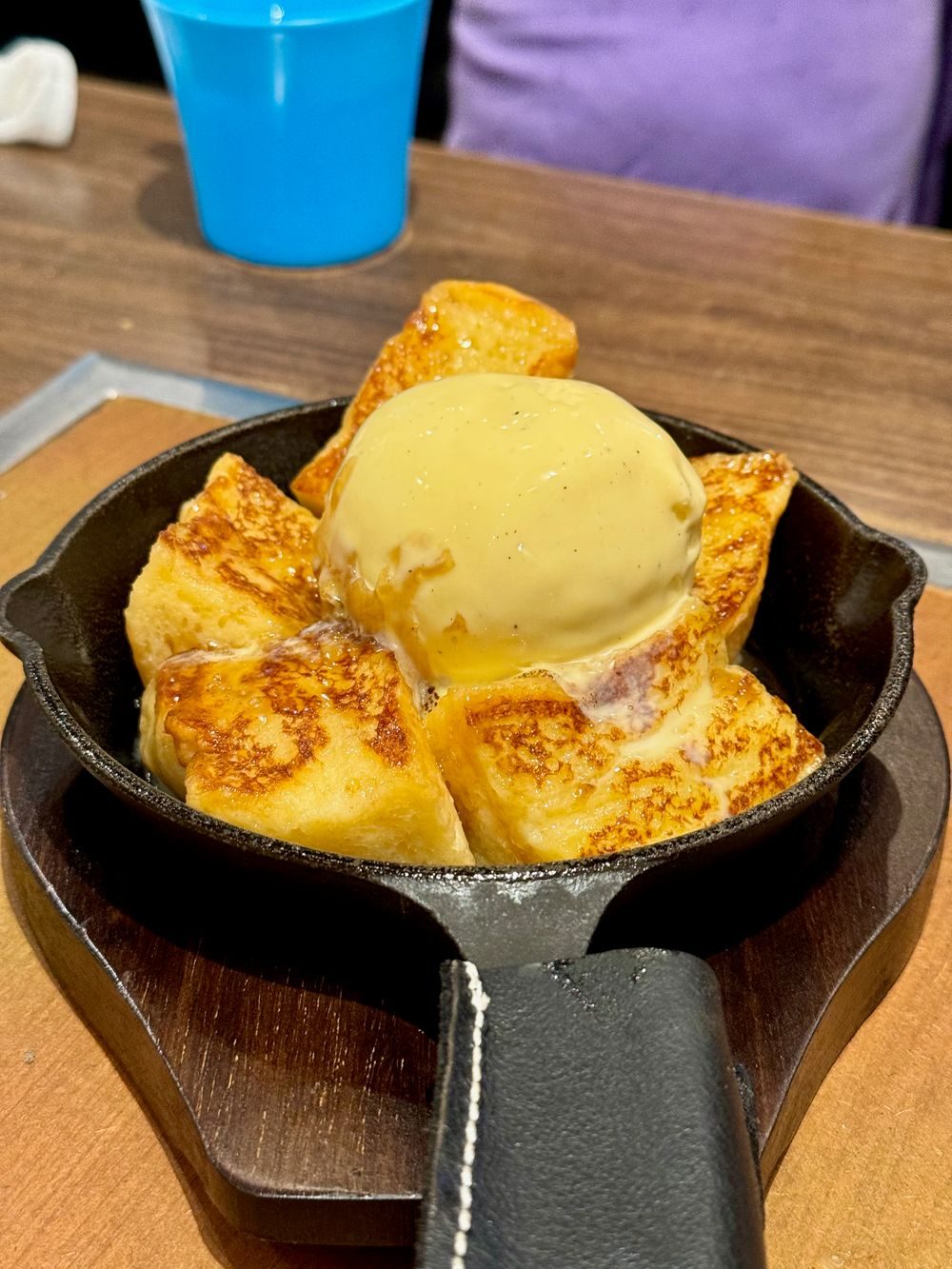 Grilled French toast slices topped with a scoop of ice cream, served in a small iron skillet with a wooden handle.