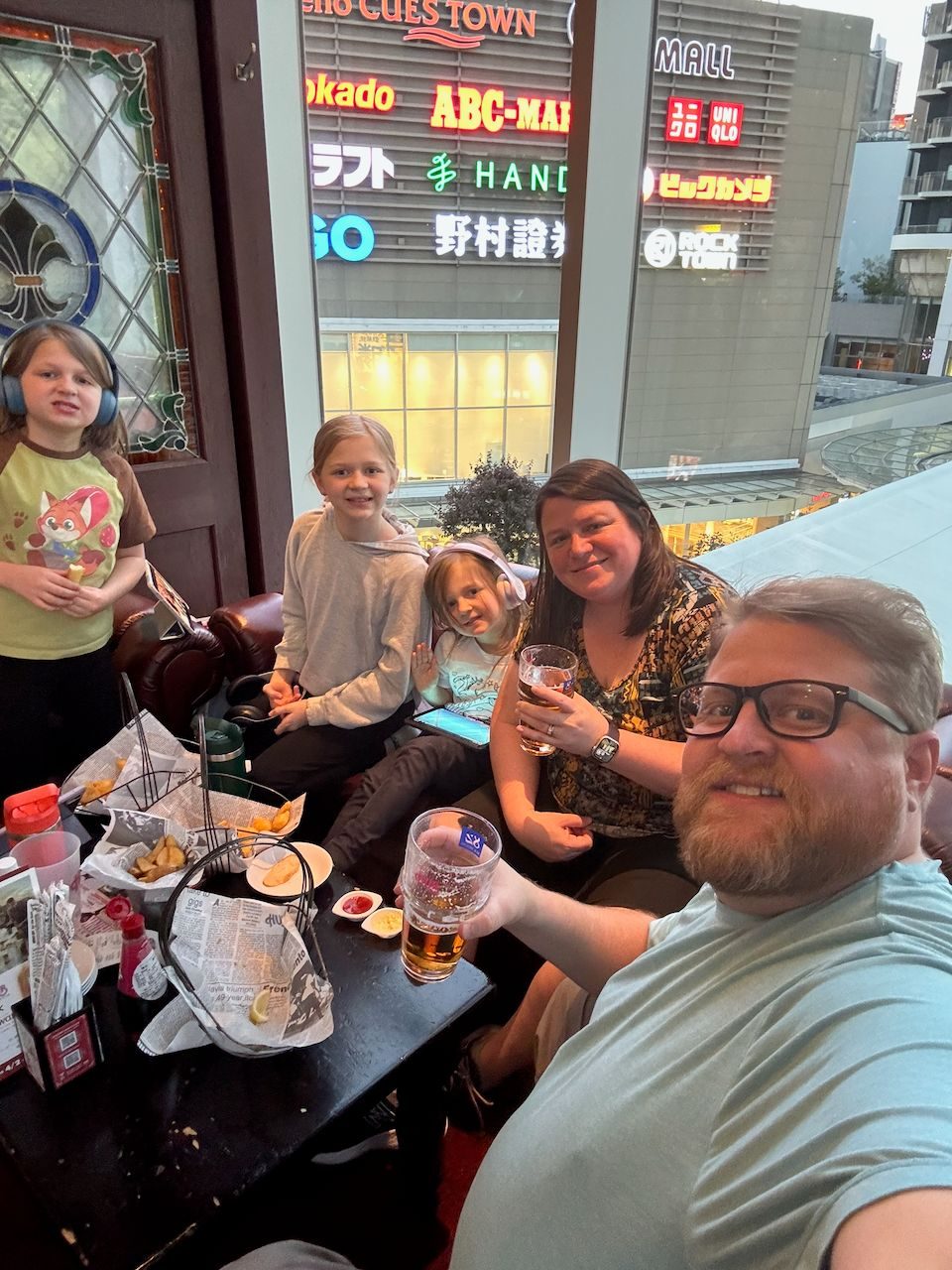 The Clarkson family at a pub table in Osaka with neon shopping signs visible through the window behind them