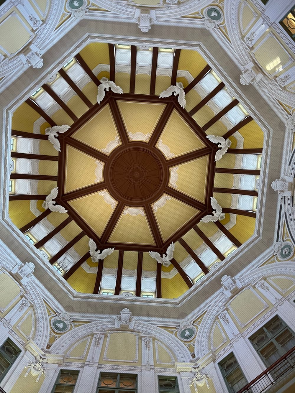A view straight up into one of Tokyo Station's restored octagonal dome ceilings, showing ornate cream and gold relief work radiating from a central medallion.