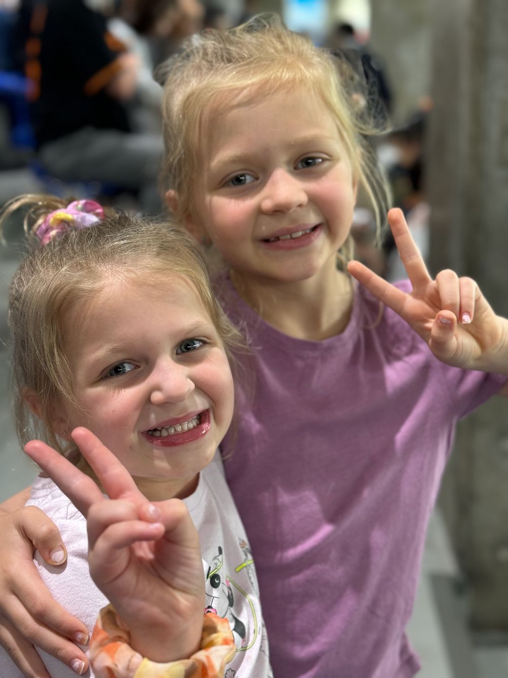 Two young girls make peace signs for a selfie at Tokyo Dome, with fans visible in the background.